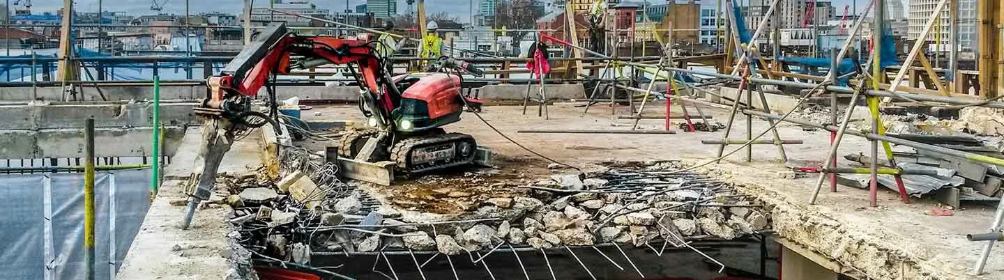 A DEMSO remote-controlled demolition machine breaking out a reinforced concrete slab on a city rooftop